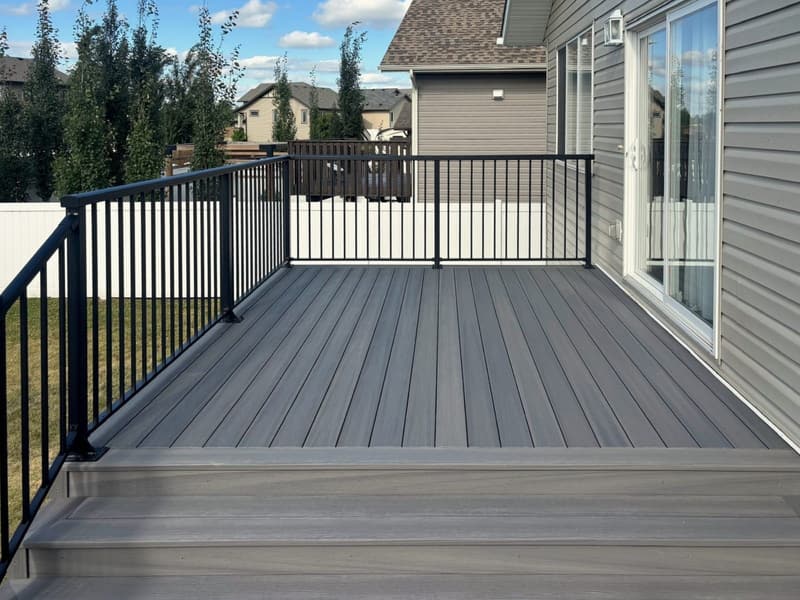 A grey composite deck with a black aluminum railing, two wide steps down to the lawn and a sliding door into the house