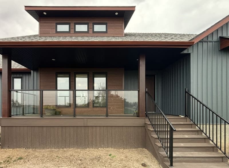 A covered front porch with a glass railing, black metal stair rails and a composite deck