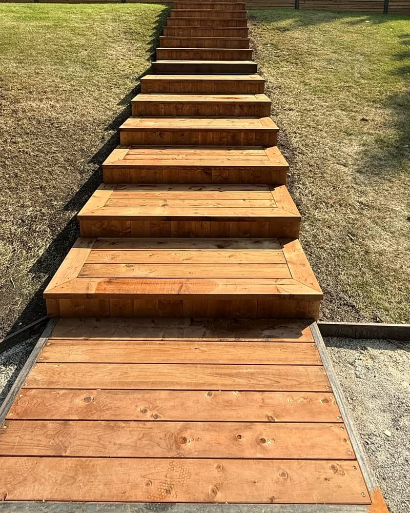 Wood steps built down a grassy slope in a backyard, ending on a wood landing